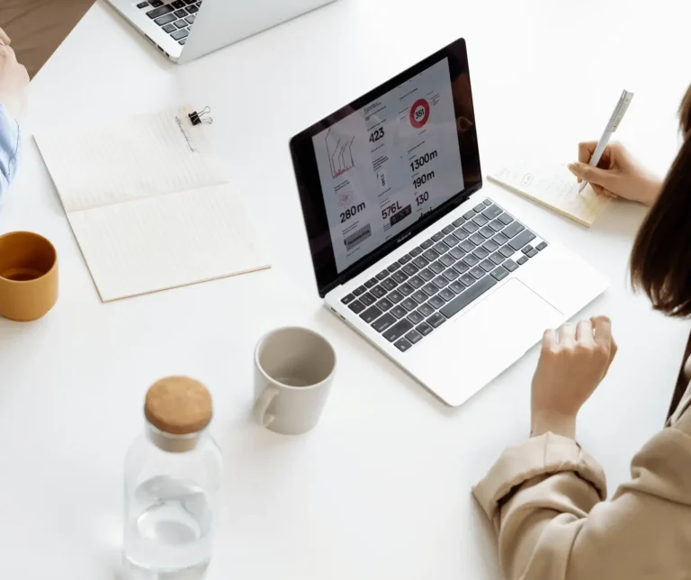 Woman taking notes beside a laptop at a work desk