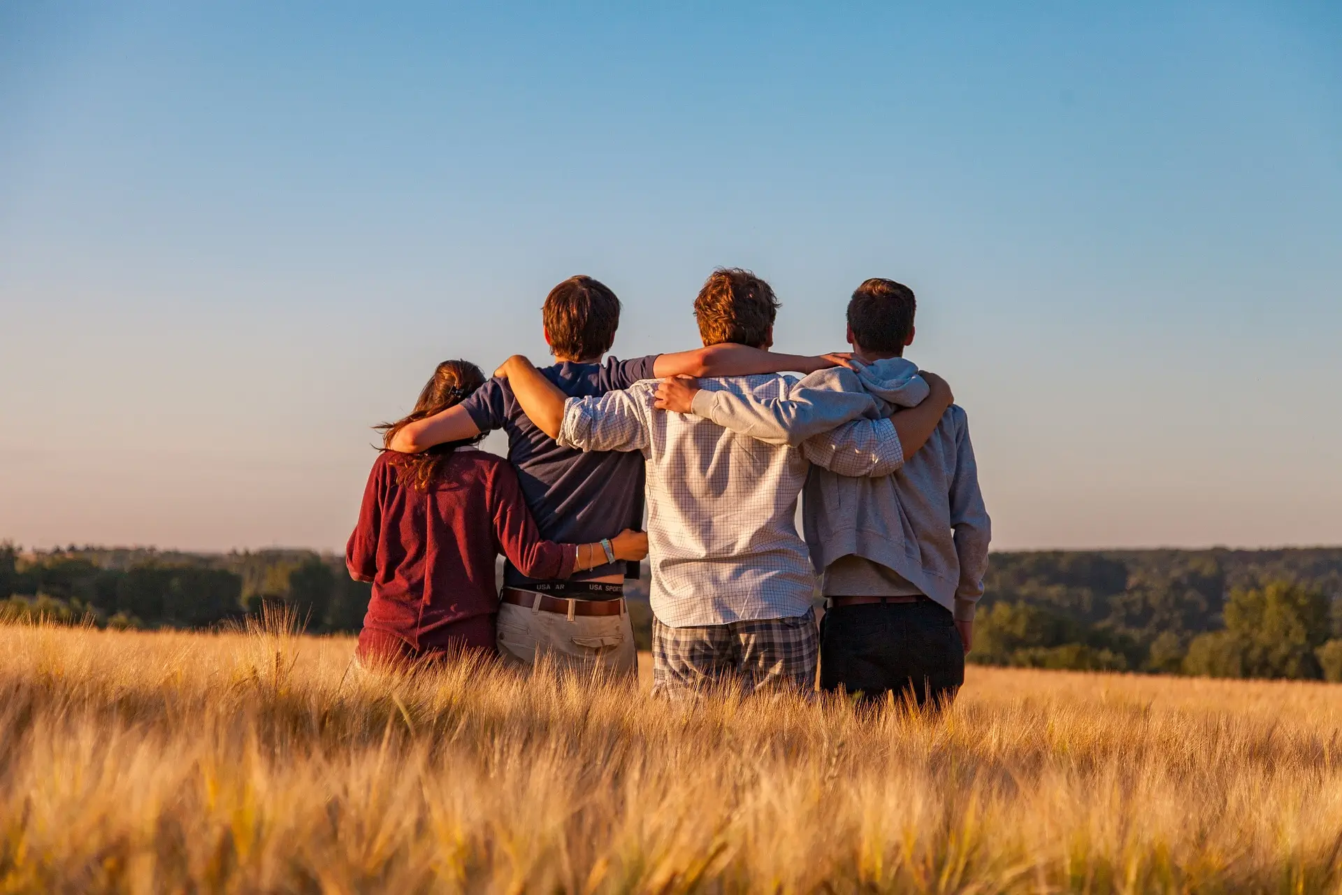 Group of friends with arms around each other in a golden field